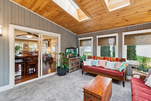living area with a ceiling fan, carpet, lofted ceiling with skylight, and wooden walls