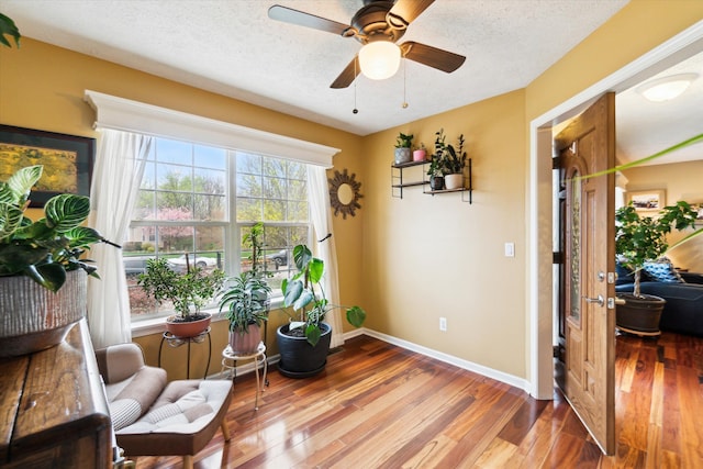 living area featuring baseboards, ceiling fan, a textured ceiling, and wood finished floors