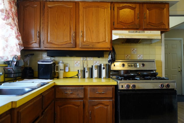 20115 Santa Barbara Dr, Detroit, MI 48221 - kitchen with under cabinet range hood, stainless steel gas range, light countertops, brown cabinets, and decorative backsplash