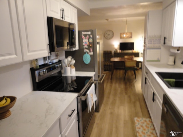 kitchen featuring light wood finished floors, light stone counters, a sink, appliances with stainless steel finishes, and white cabinetry