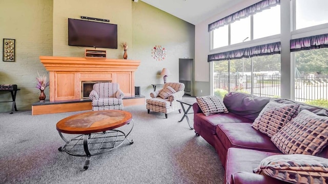 living area featuring carpet floors, high vaulted ceiling, and a fireplace with raised hearth
