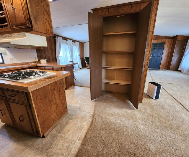 kitchen featuring under cabinet range hood, wooden walls, white gas cooktop, wood counters, and light colored carpet