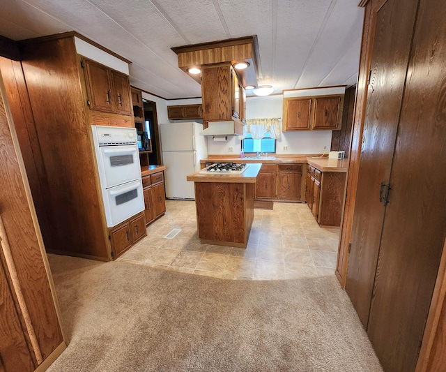 kitchen featuring light countertops, white appliances, brown cabinetry, a kitchen island, and light carpet