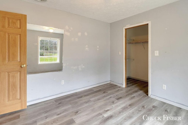 unfurnished bedroom with a textured ceiling, a closet, a walk in closet, light wood finished floors, and baseboards