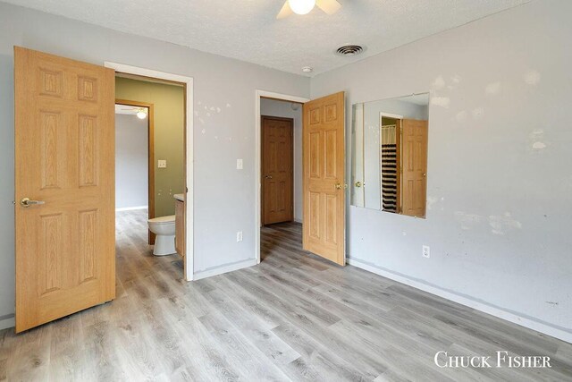 unfurnished bedroom featuring visible vents, connected bathroom, light wood-type flooring, baseboards, and a textured ceiling