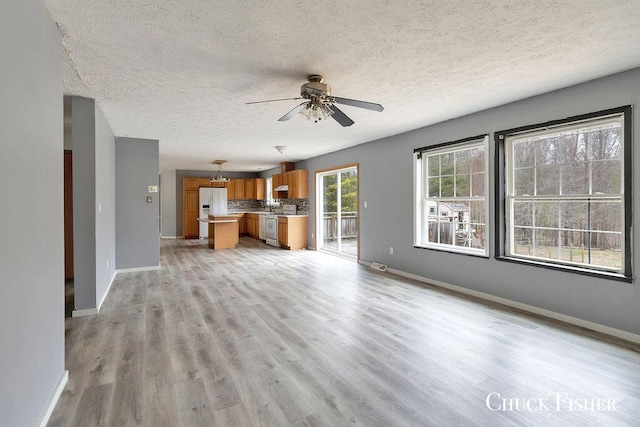 unfurnished living room with light wood-type flooring, a textured ceiling, baseboards, and ceiling fan