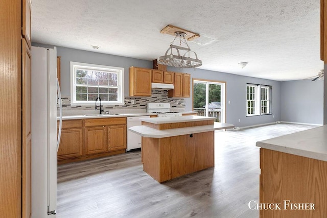 kitchen with a sink, white appliances, light wood-style floors, a center island, and a textured ceiling