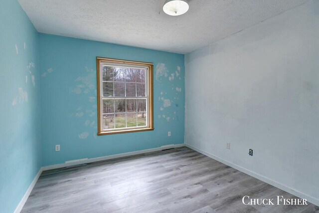 empty room with baseboards, wood finished floors, and a textured ceiling