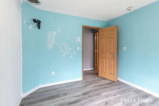 spare room featuring a textured ceiling, wood finished floors, visible vents, and baseboards