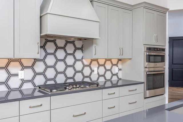 kitchen featuring tasteful backsplash, white cabinets, appliances with stainless steel finishes, dark countertops, and custom range hood