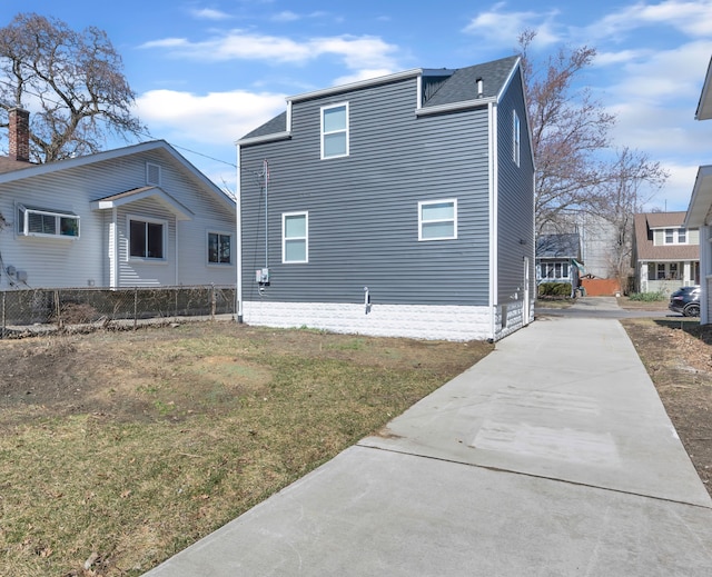 view of side of property featuring concrete driveway, a yard, fence, and a shingled roof