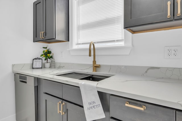 kitchen featuring gray cabinets, light stone counters, stainless steel dishwasher, and a sink