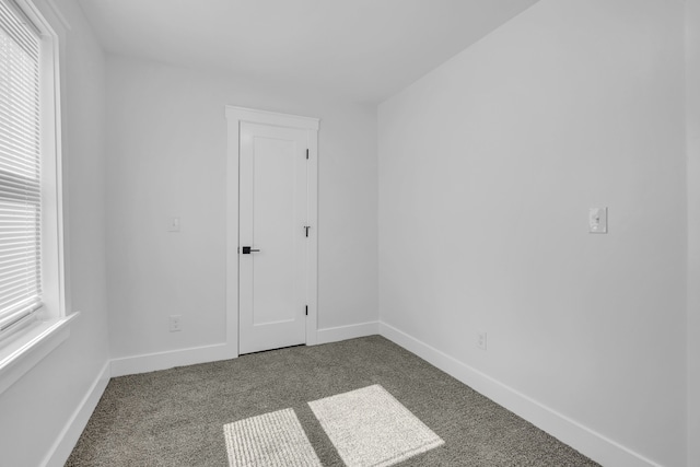 empty room featuring baseboards and dark carpet