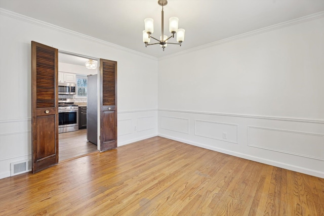 spare room featuring ornamental molding, visible vents, light wood finished floors, and a notable chandelier