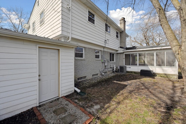rear view of property with cooling unit, a sunroom, and a chimney