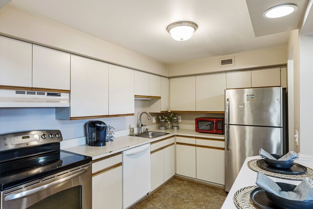 kitchen with stainless steel appliances, under cabinet range hood, a sink, light countertops, and white cabinetry
