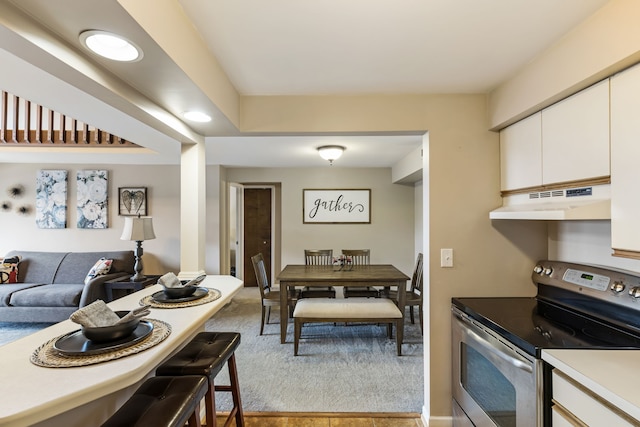 kitchen featuring stainless steel electric stove, under cabinet range hood, light colored carpet, light countertops, and white cabinetry