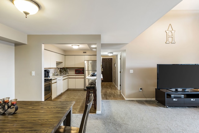 kitchen featuring appliances with stainless steel finishes, a sink, carpet flooring, white cabinetry, and baseboards