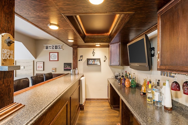bar featuring a raised ceiling, baseboards, dark wood finished floors, and crown molding