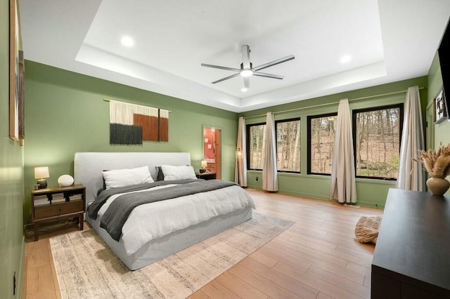 bedroom with multiple windows, wood finished floors, and a raised ceiling
