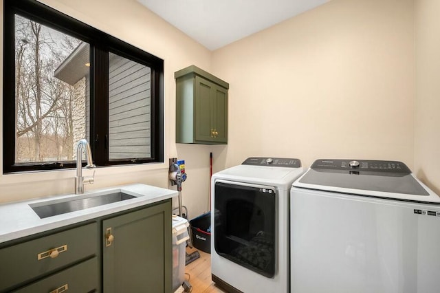 clothes washing area with a sink, a wealth of natural light, light wood-type flooring, cabinet space, and washing machine and clothes dryer