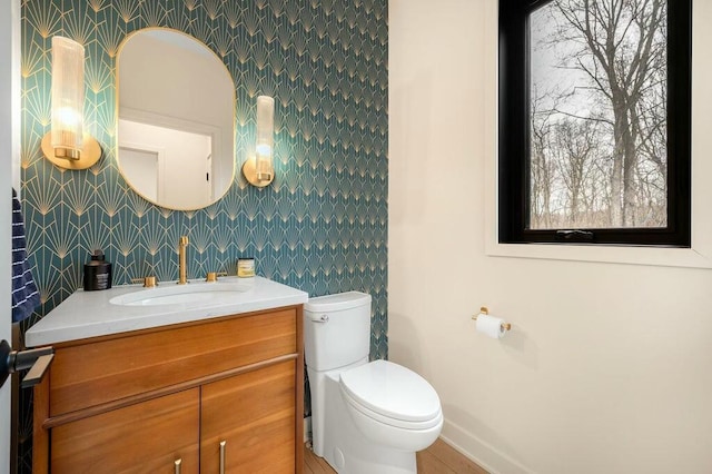 half bath featuring toilet, wallpapered walls, vanity, and baseboards