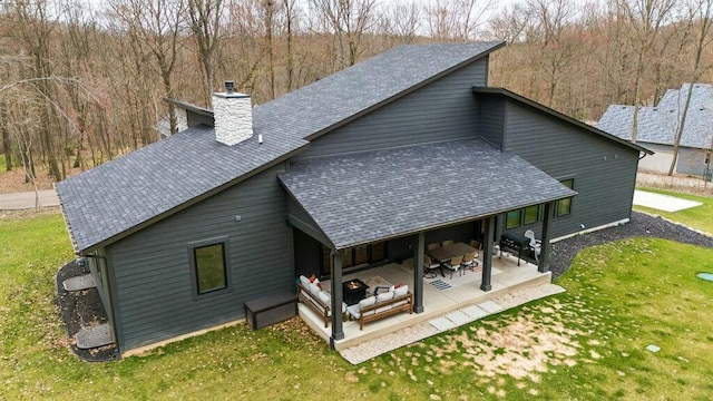 rear view of house featuring a patio area, a shingled roof, a lawn, and a chimney