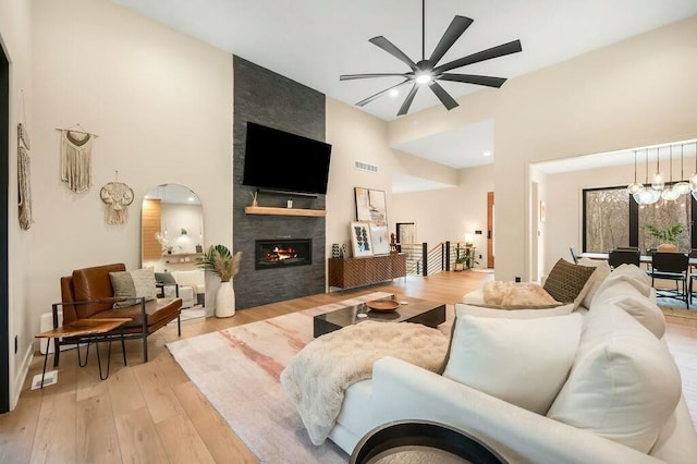 living area featuring visible vents, a ceiling fan, light wood finished floors, a towering ceiling, and a large fireplace
