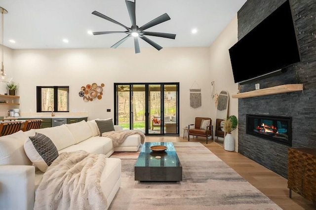 living area with a ceiling fan, a fireplace, light wood finished floors, recessed lighting, and a towering ceiling