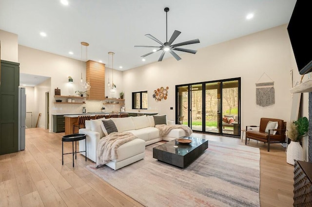 living room featuring light wood finished floors, ceiling fan, a towering ceiling, and recessed lighting