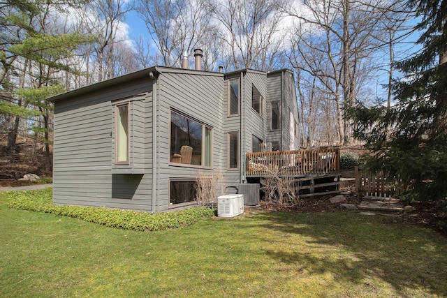 rear view of property featuring a lawn, a chimney, central AC, and a deck