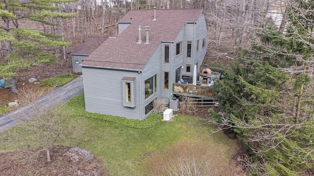 back of property with a chimney, roof with shingles, a yard, and a deck