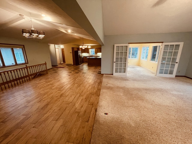unfurnished living room with lofted ceiling, wood finished floors, baseboards, and an inviting chandelier