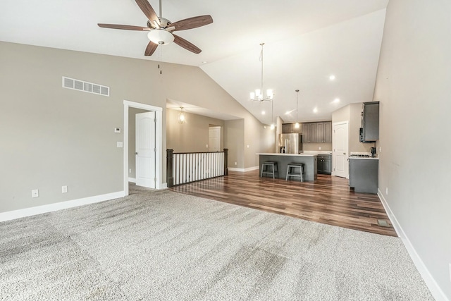 unfurnished living room with dark carpet, ceiling fan with notable chandelier, baseboards, and visible vents