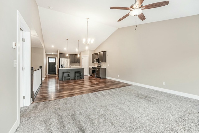 unfurnished living room featuring baseboards, dark colored carpet, dark wood-style floors, vaulted ceiling, and ceiling fan with notable chandelier