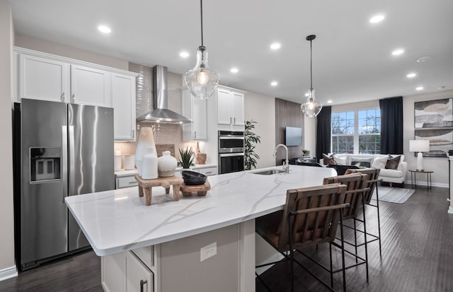 kitchen with wall chimney range hood, recessed lighting, white cabinetry, stainless steel appliances, and a sink