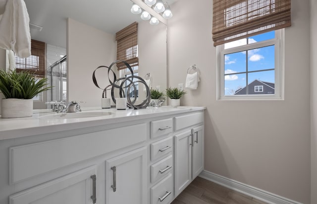 full bath with wood finished floors, a sink, a stall shower, double vanity, and baseboards