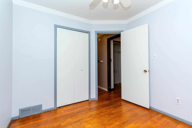 unfurnished bedroom featuring visible vents, a closet, ornamental molding, a ceiling fan, and wood finished floors