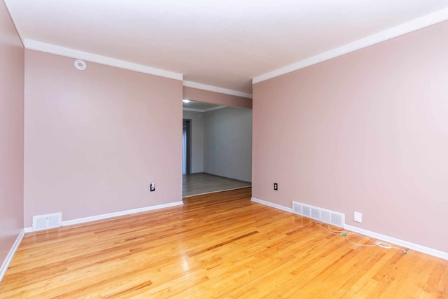 spare room featuring wood finished floors, baseboards, ornamental molding, and visible vents