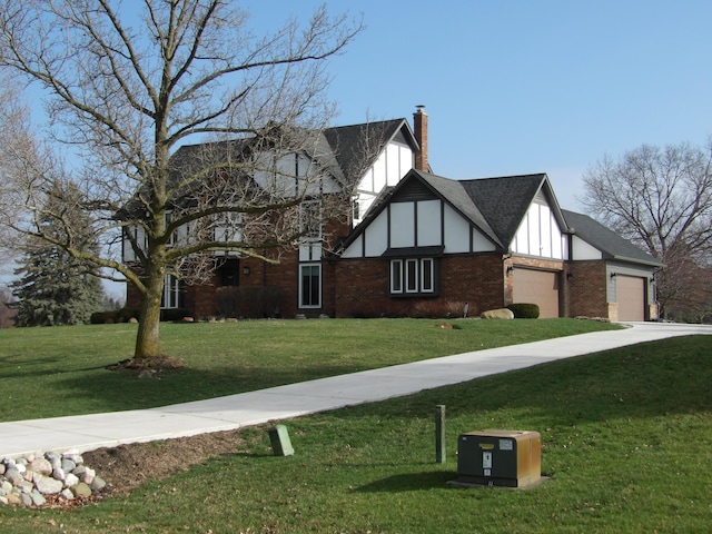 tudor home with board and batten siding, roof with shingles, a front yard, brick siding, and a garage