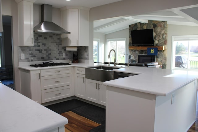 kitchen featuring tasteful backsplash, wall chimney range hood, light countertops, black gas stovetop, and a sink