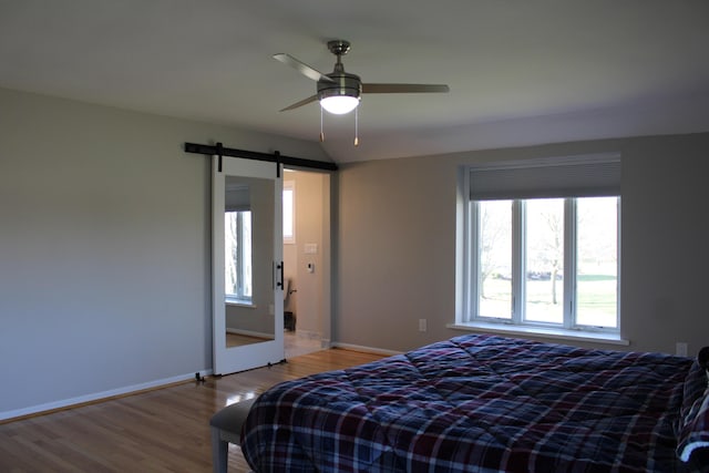 bedroom with baseboards, a ceiling fan, a barn door, and wood finished floors
