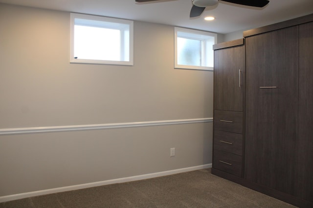 unfurnished bedroom with a ceiling fan, dark colored carpet, multiple windows, and baseboards