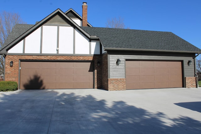 english style home featuring a garage, brick siding, a chimney, a shingled roof, and concrete driveway