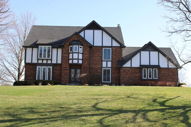 tudor home featuring roof with shingles, french doors, a front yard, and brick siding