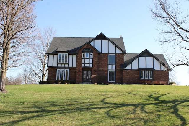 tudor house with brick siding, a front lawn, and roof with shingles