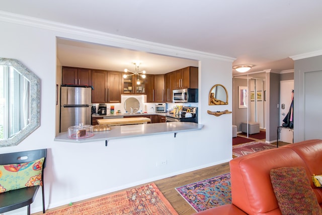 1050 Wall St Unit 3C, Ann Arbor, MI 48105 - kitchen with appliances with stainless steel finishes, a peninsula, wood finished floors, crown molding, and a chandelier