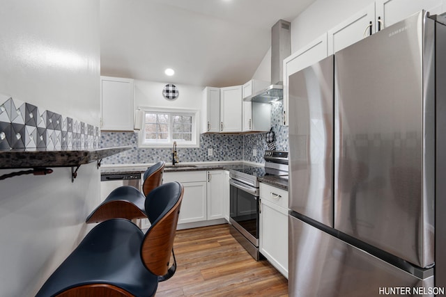 175 Cora Ave, Muskegon, MI 49445 - kitchen featuring dark countertops, wall chimney exhaust hood, appliances with stainless steel finishes, light wood finished floors, and a sink