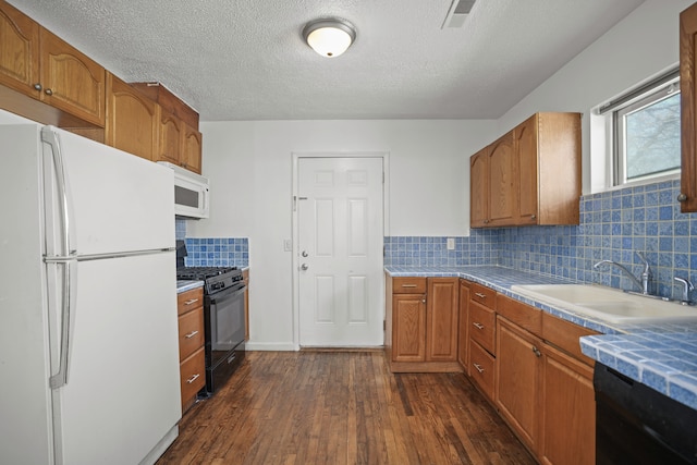 kitchen with visible vents, a sink, decorative backsplash, black appliances, and dark wood-style flooring