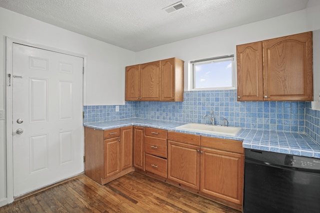 kitchen with dark wood finished floors, visible vents, dishwasher, a sink, and tile counters